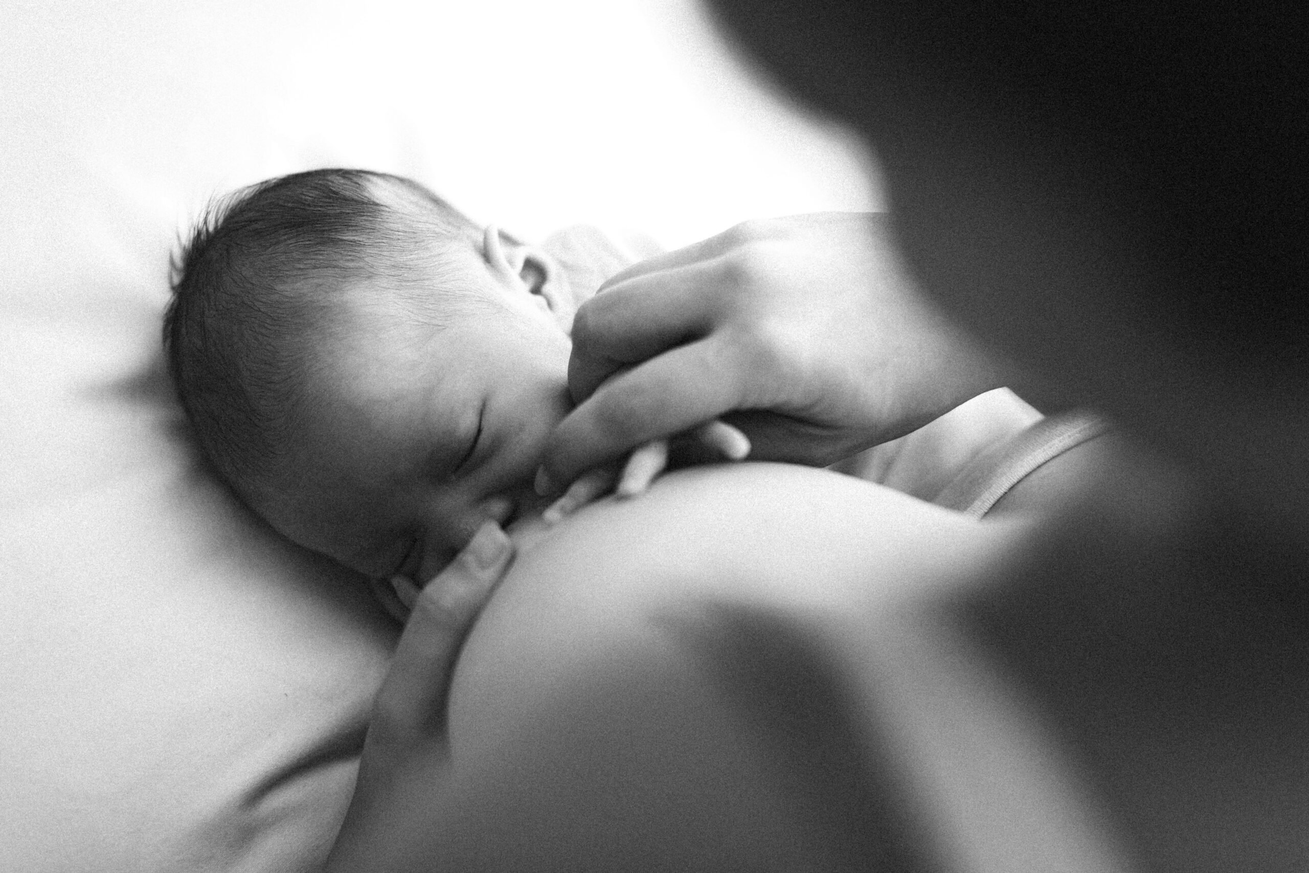 Mother breastfeeding a newborn with baby held close at the breast